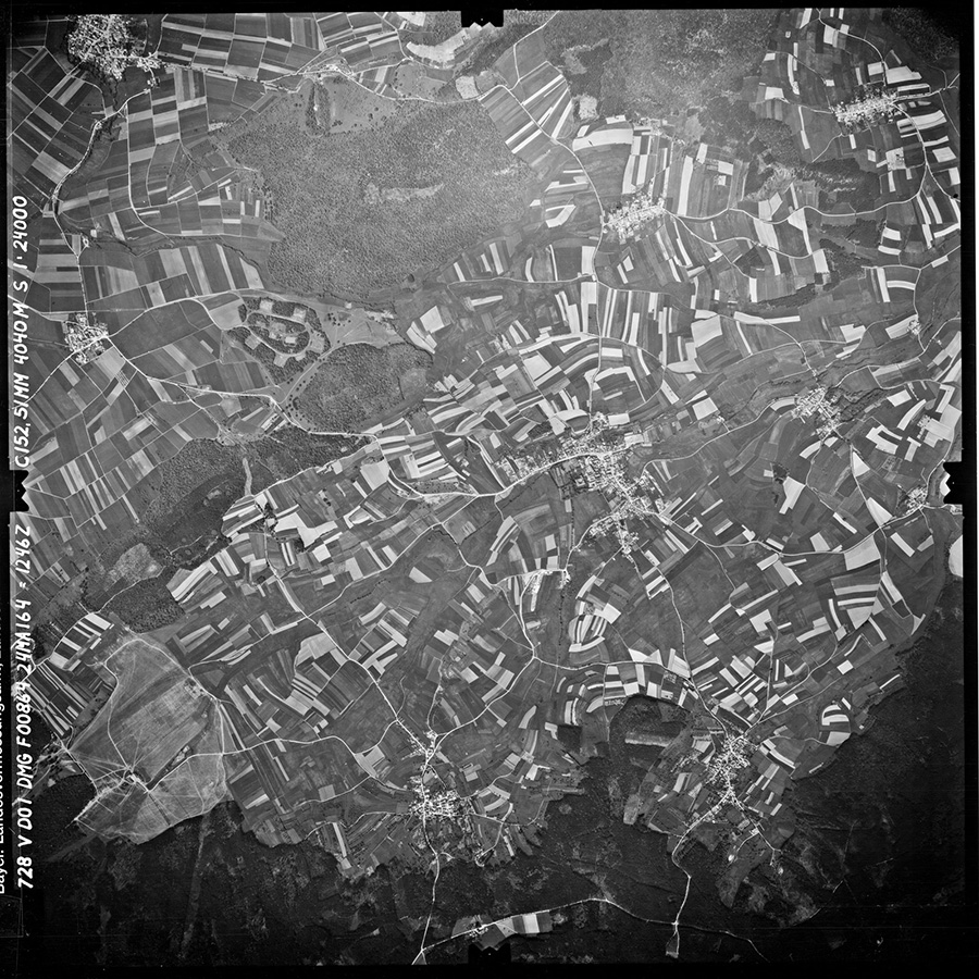 Eine schwarz-weiß Luftbildaufnahme zeigt Wiesen und Felder.