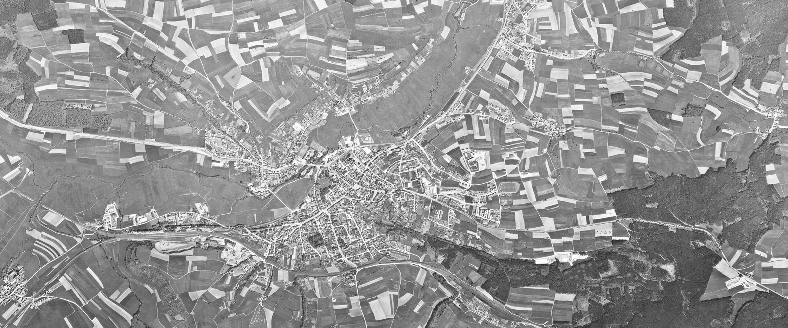 Die schwarz-weiß Luftbildaufnahme zeigt Wiesen Felder, Straßen und Gebäude.