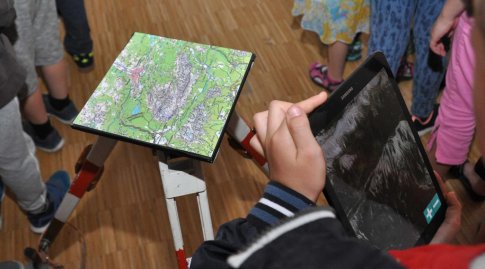 Mehrere Kinder stehen um eine topographische Karte. Ein Kind bedient ein Tablet, um die Karte zu erkunden.