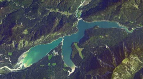 Farbluftbild das den Sylvensteinspeicher im Jahre 2020 zeigt. Der Stausee  wird von drei Flüssen gespeist und liegt in bewaldeter Umgebung.