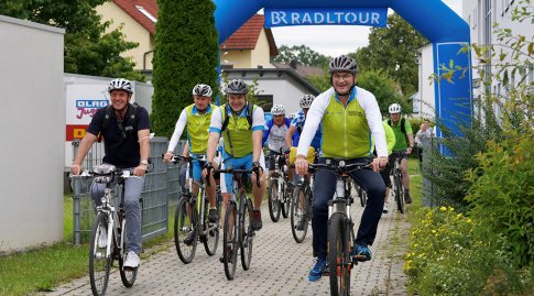 Die geladenen Gäste der Ersatzveranstaltung der BR-Radltour 2021 starten mit ihren Fahrrädern durch das Starttor des Bayerischen Rundfunks. Die abgebildeten Personen werden in der Bildunterschrift genannt.